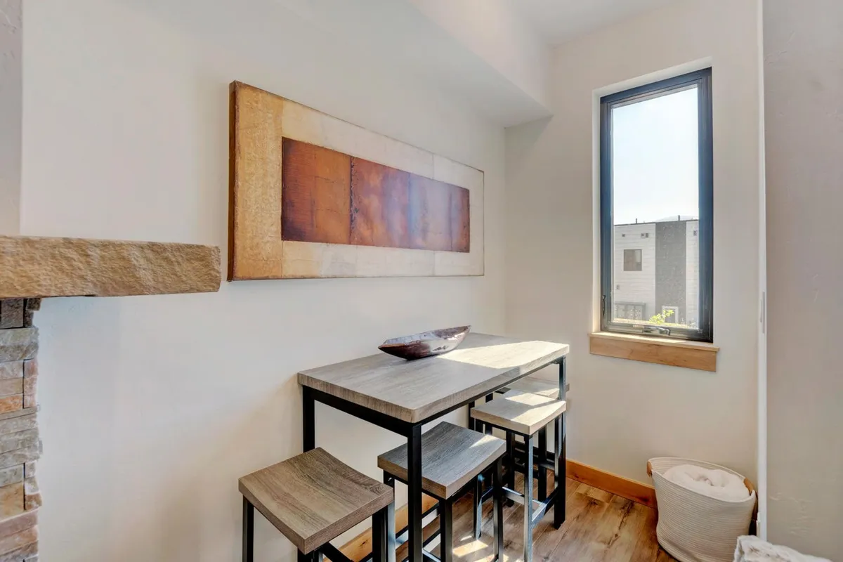 A wooden dining table set near a window, bathed in natural light and complemented by minimalist decor. The intimate setting is perfect for meals or morning coffee.