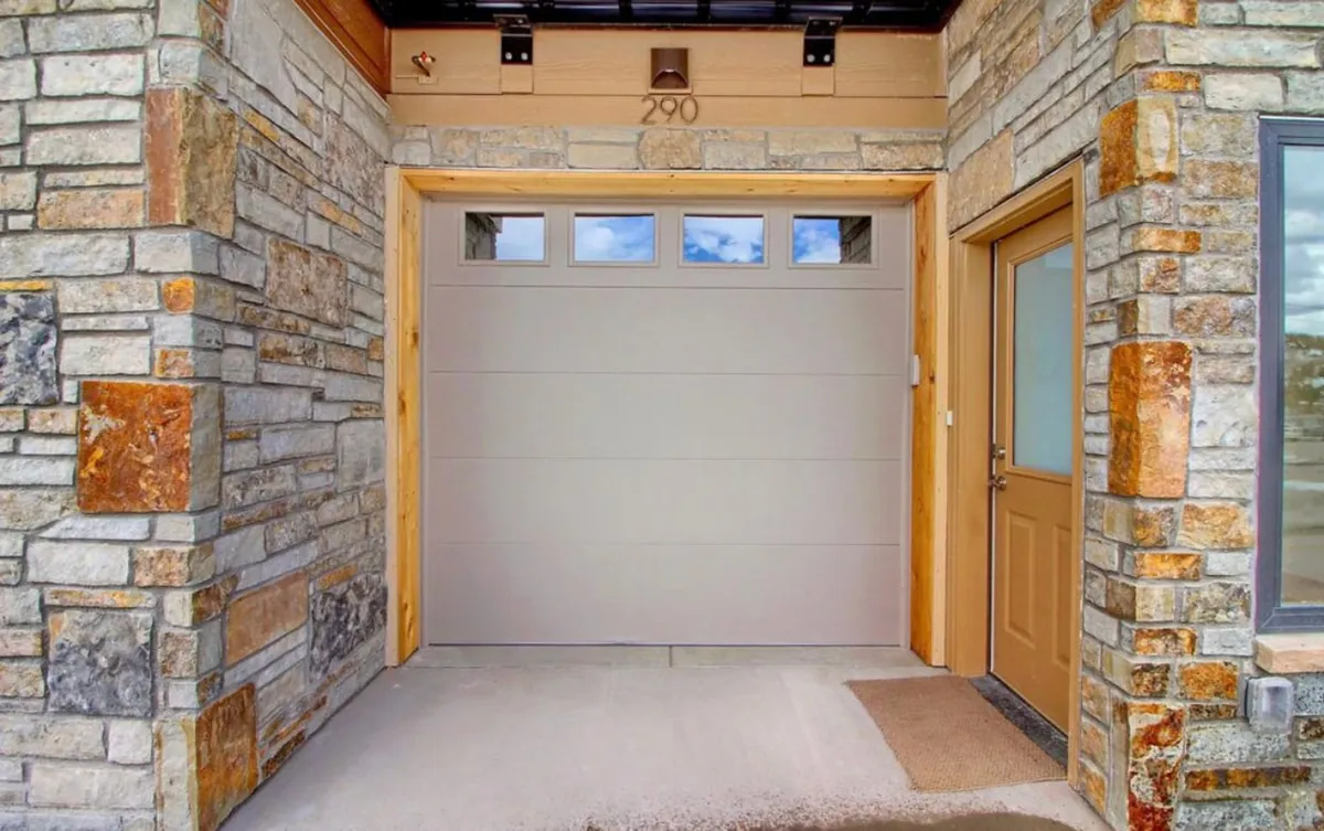 The inviting front entrance and stone façade of the luxury townhome, featuring the garage with EV charging and a number plaque. The image emphasizes an upscale arrival experience, highlighting both the exclusivity and accessibility of the property.