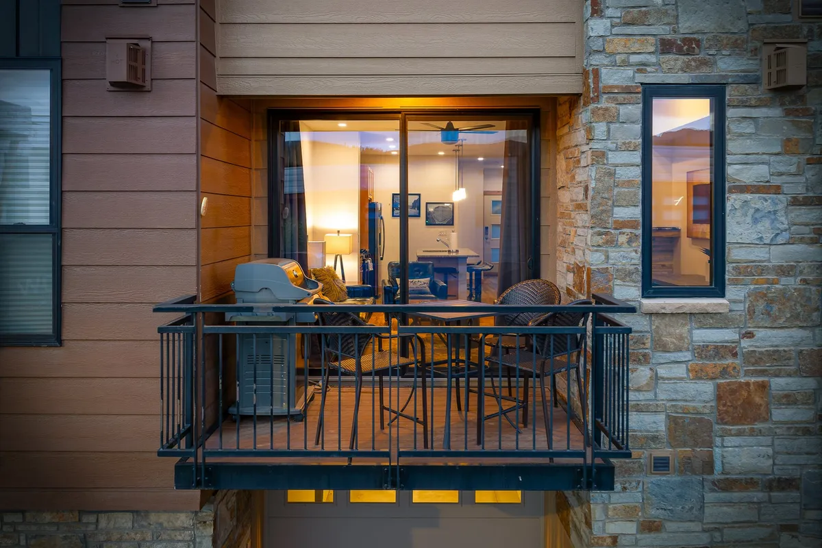A stylish balcony with a gas grill, outdoor seating, and warm interior lighting visible through the windows. The setting is ideal for barbecuing, outdoor dining, and enjoying morning coffee with mountain views, reinforcing the connection between indoor comfort and outdoor luxury.