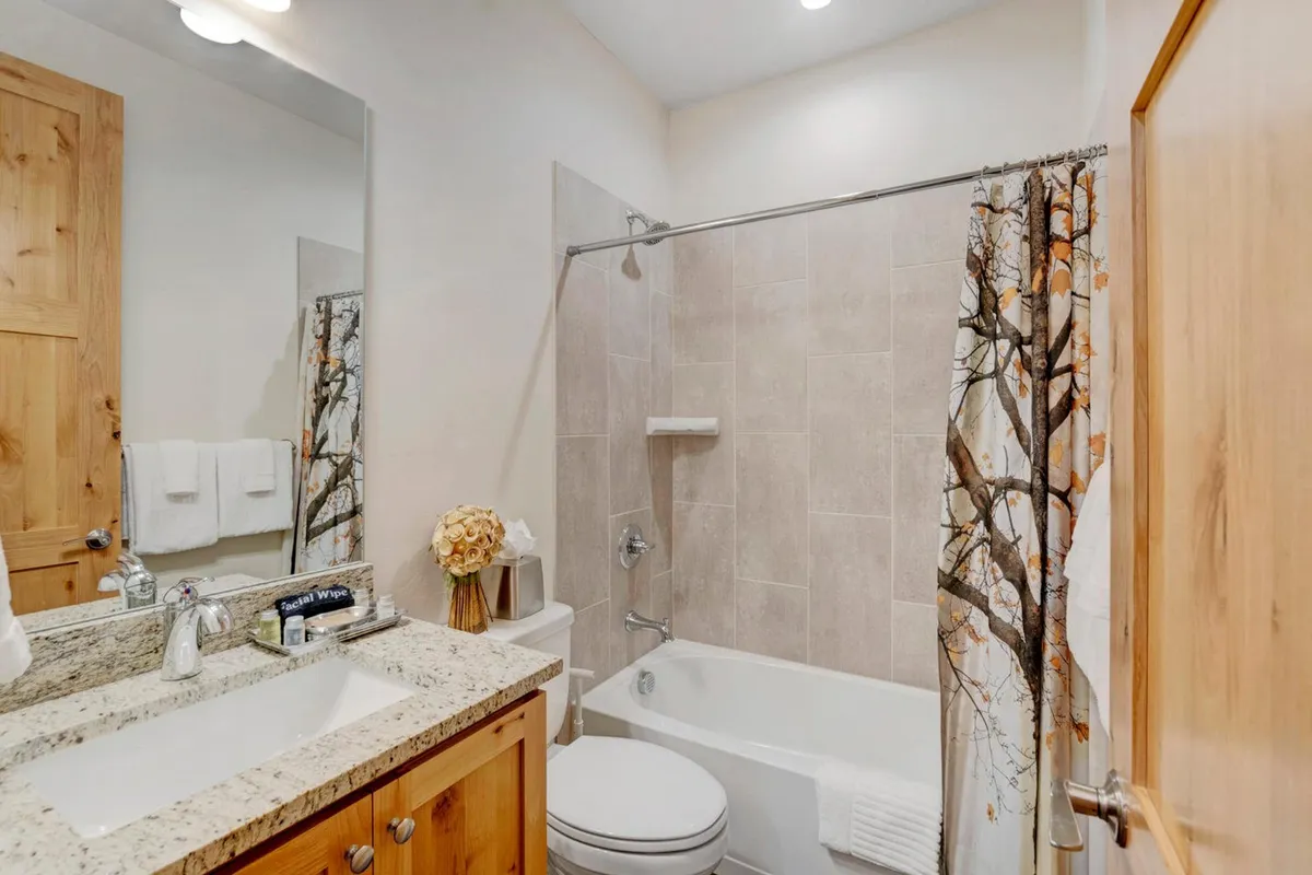 A serene bathroom featuring a granite countertop, a decorative shower curtain with a tree design, and a well-lit mirror. The ambiance is calming and spa-like, with natural light enhancing the peaceful setting.