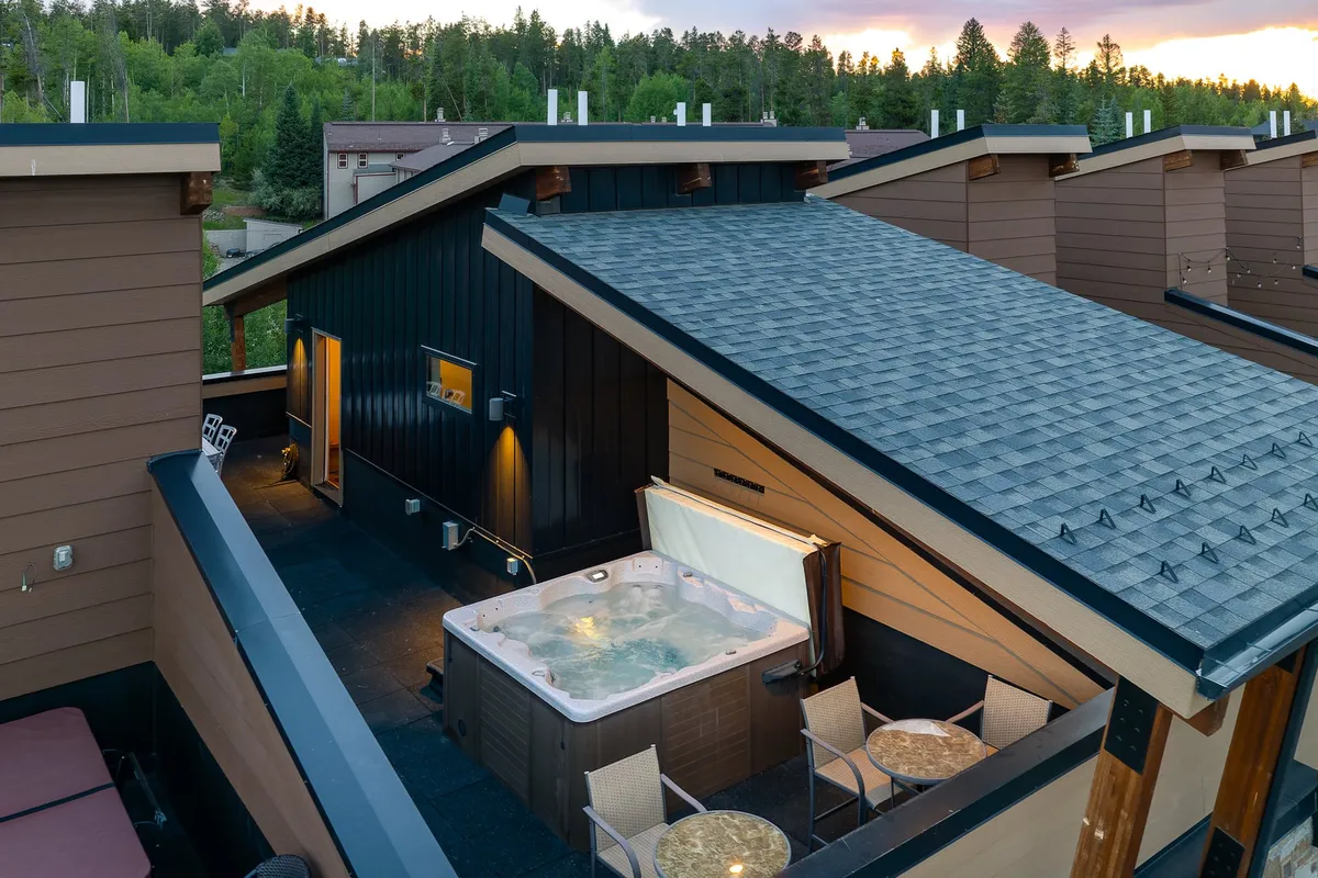 An outdoor hot tub with comfortable seating is set amidst surrounding trees, offering privacy and a tranquil atmosphere. The scene captures the luxury of relaxing in a hot tub while taking in the beautiful natural environment, with hints of mountain vistas in the background.
