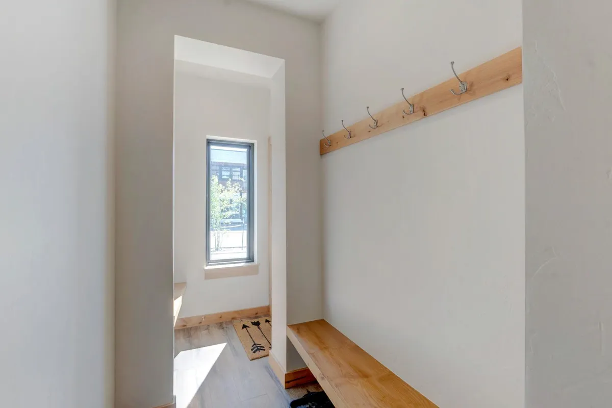 An inviting mudroom or entry area featuring a window, wooden bench, and prominent coat hooks. The space is set up for guests to stow jackets, boots, and outdoor gear, making it the natural transition zone between adventure and home comforts.