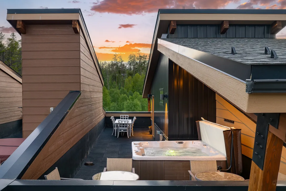 A tranquil exterior setting featuring a hot tub, dining area, and sunset sky framed by trees. This scene captures guests relaxing in the hot tub or enjoying dinner outdoors as the day transitions to night.