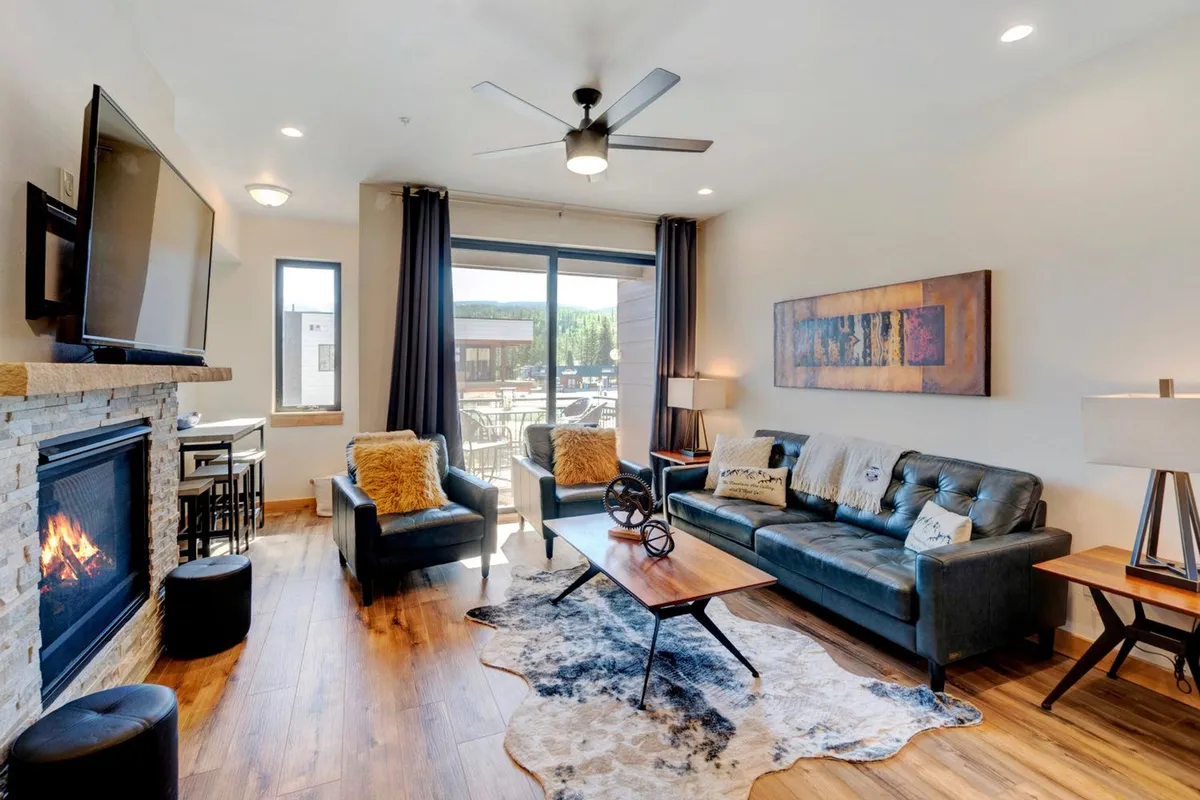 A comfortable living room centered around a stone fireplace, with a soft sofa, coffee table, and a large window letting in natural light. The mood is inviting, perfect for relaxing, reading, or evening entertainment.