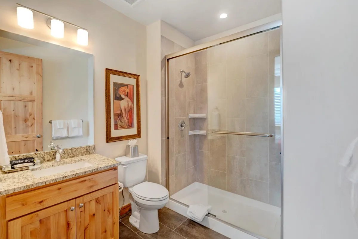 A bathroom with a spacious granite countertop, wooden cabinets, a glass-enclosed shower, and soft lighting. The vibe is serene and modern, ideal for unwinding and self-care routines.